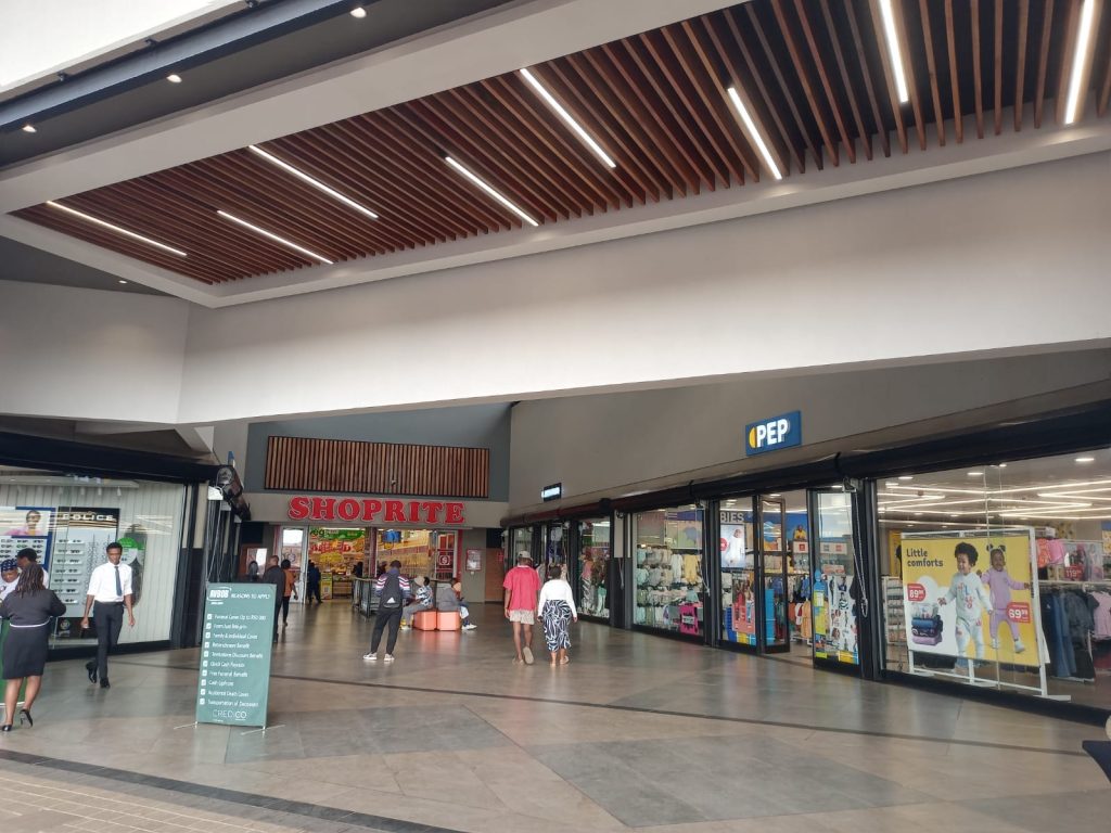 Retail corridor showing stores and shoppers inside Dhlamini Junction
